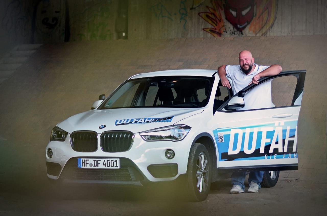 DU FÄHRST Mitarbeiter an einem gebrandeten Fahrschulfahrzeug